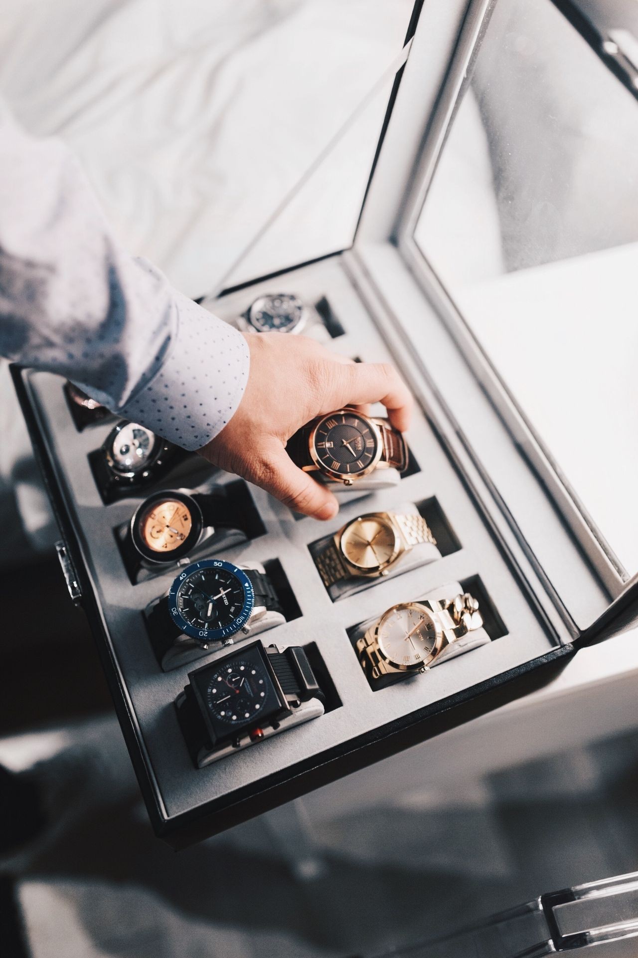 Hand selecting a watch from a box displaying various luxury watches on soft cushions.